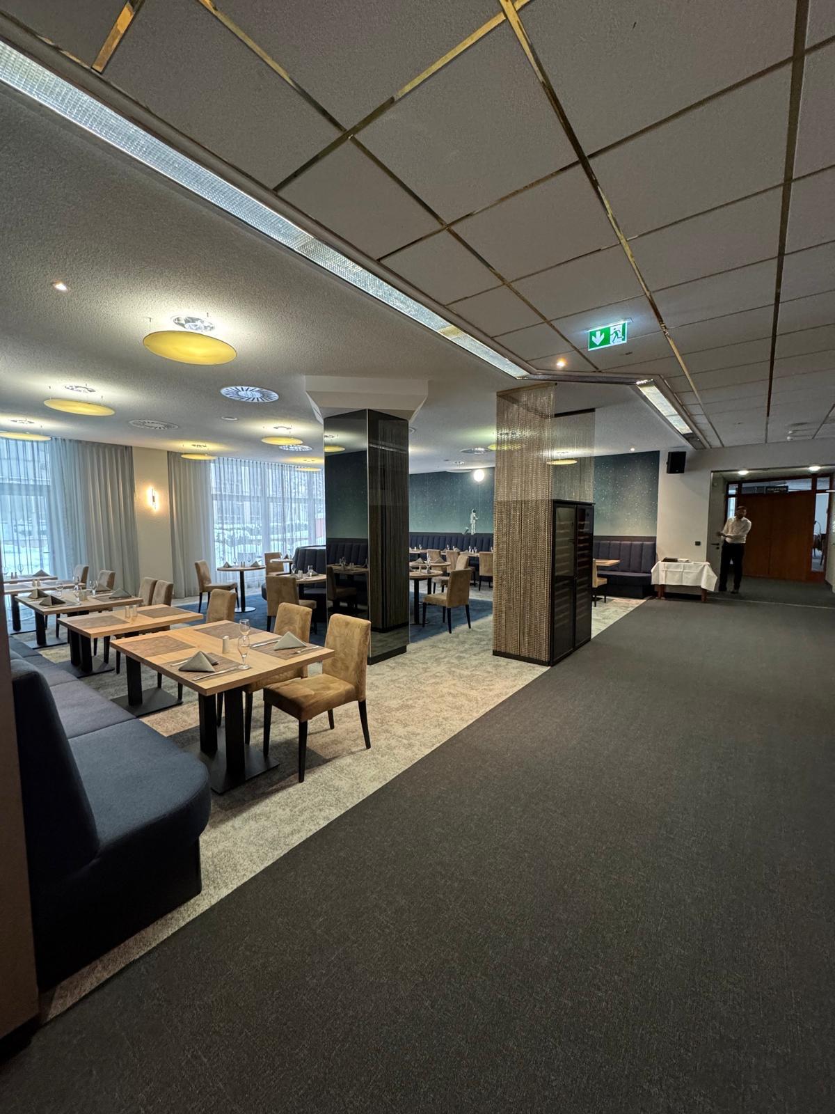 Ein elegantes Restaurant mit gedeckten Tischen, beigen Stühlen und einem Kellner am Eingang